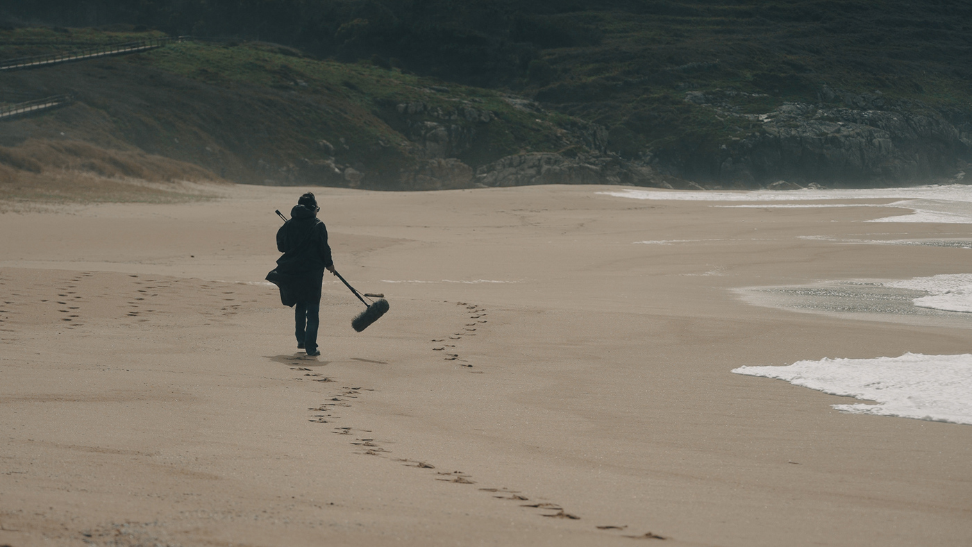 Un home cun micrófono de pértiga pasea pola praia mentres grava os sons